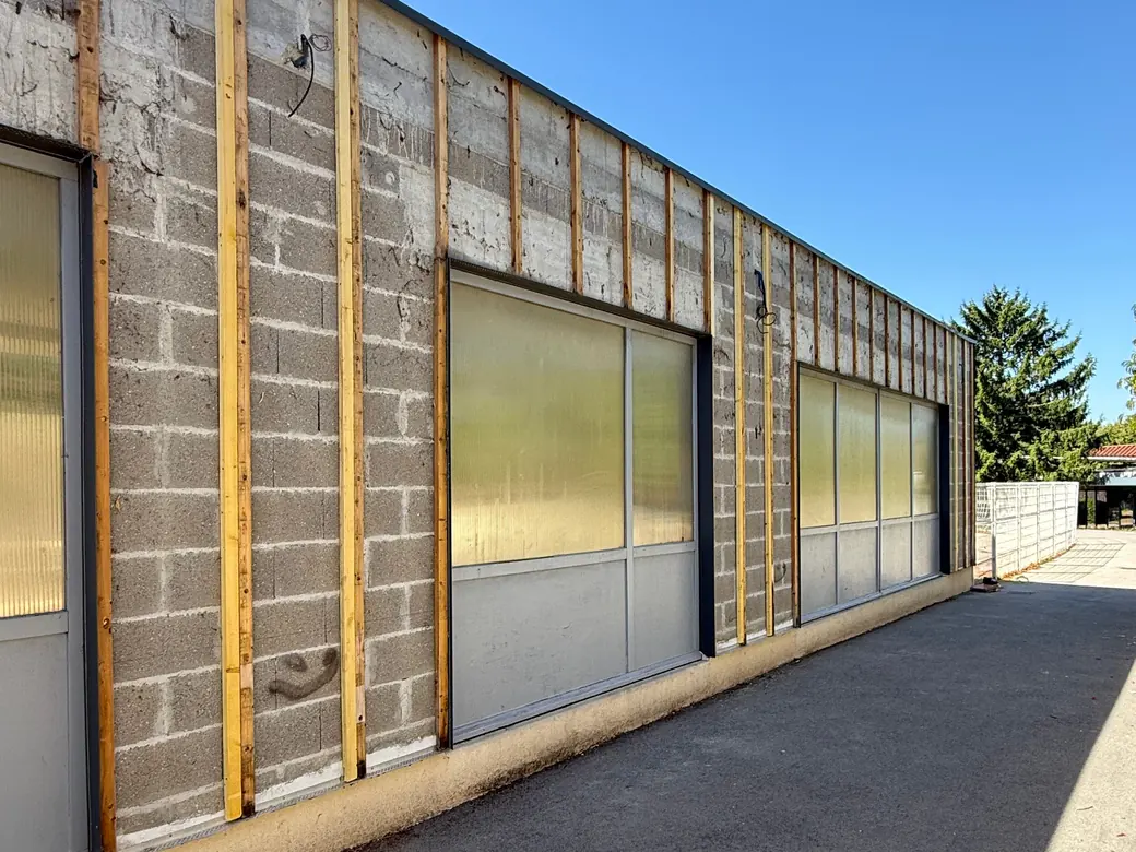 École de Viriat pendant les travaux : ancien bardage déposé, ossature bois sur le mur en parpaings
