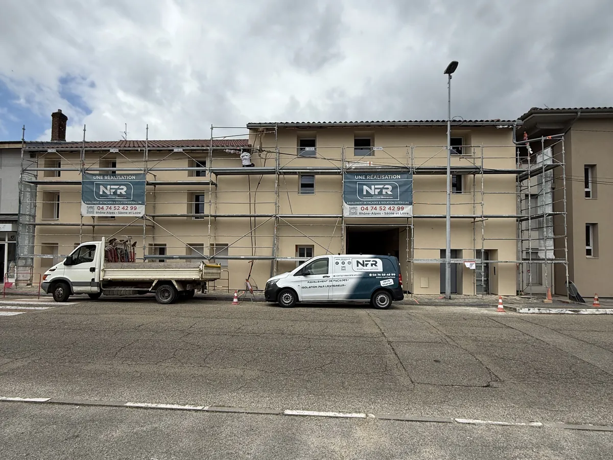 Chantier NFR d'isolation par l'extérieur à Bourg-en-Bresse : bâtiment sous échafaudage, banderoles et camions NFR