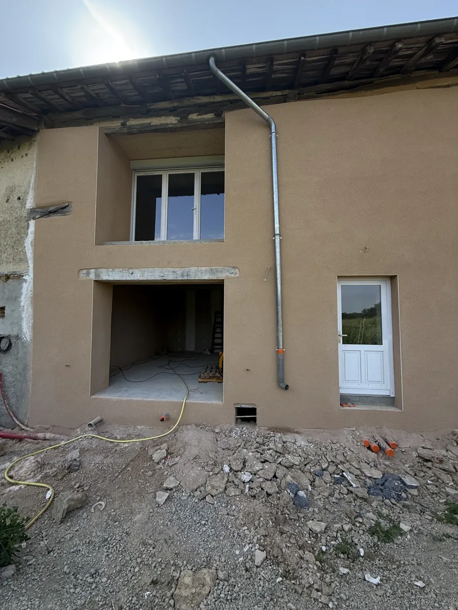 Façade de ferme en pisé fraîchement enduite en beige, ouvertures neuves, chantier NFR dans la Dombes
