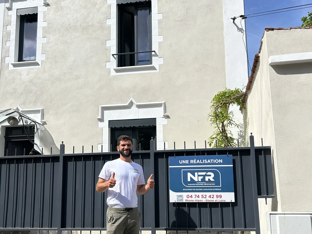 Un artisan NFR devant la façade ravalée et le panneau Une réalisation NFR