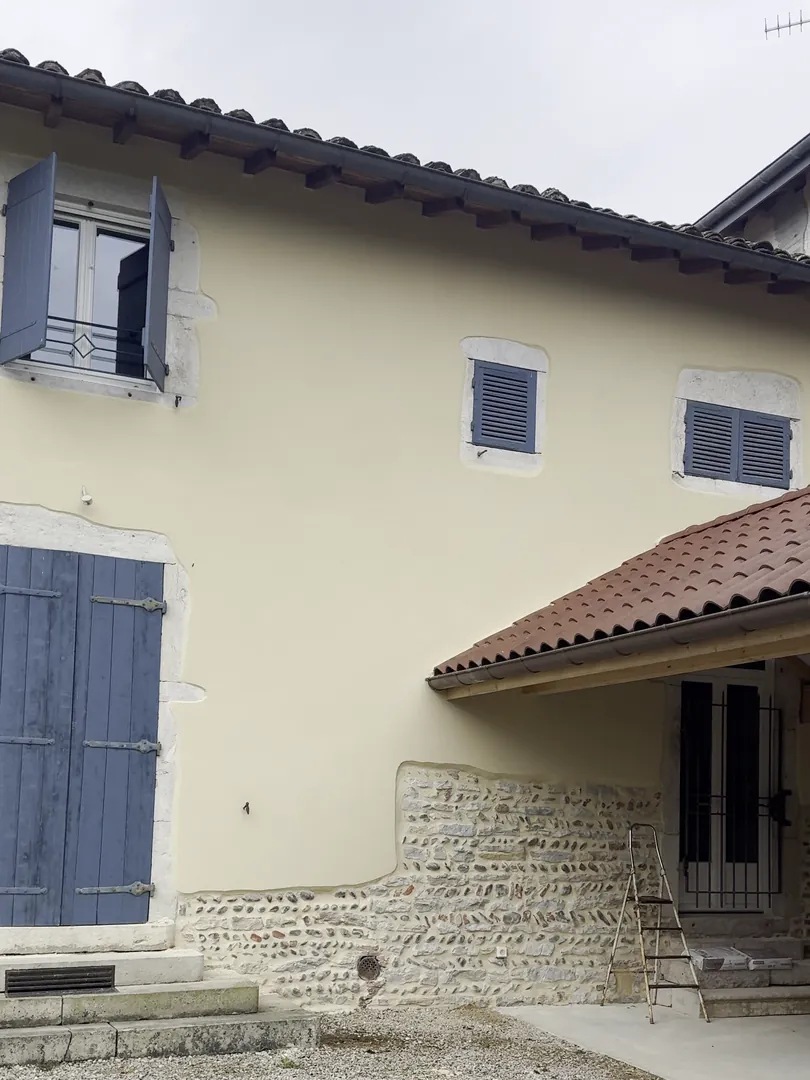 Façade enduite en beige par NFR à Buellas, volets bleus, soubassement en pierre apparent