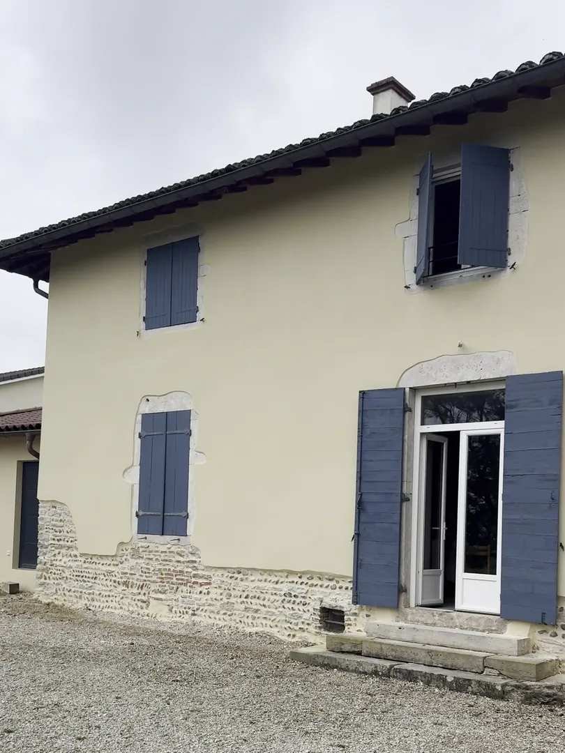 Façade d'entrée de la maison à Buellas après l'enduit NFR, volets bleus et porte-fenêtre
