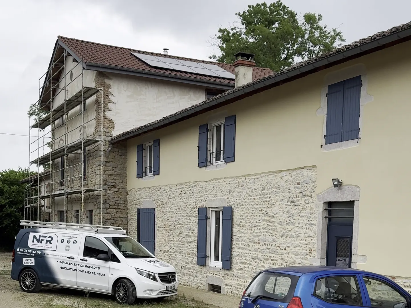 Maison en pisé à Buellas en cours de chantier, façade enduite et aile voisine sous échafaudage, camionnette NFR