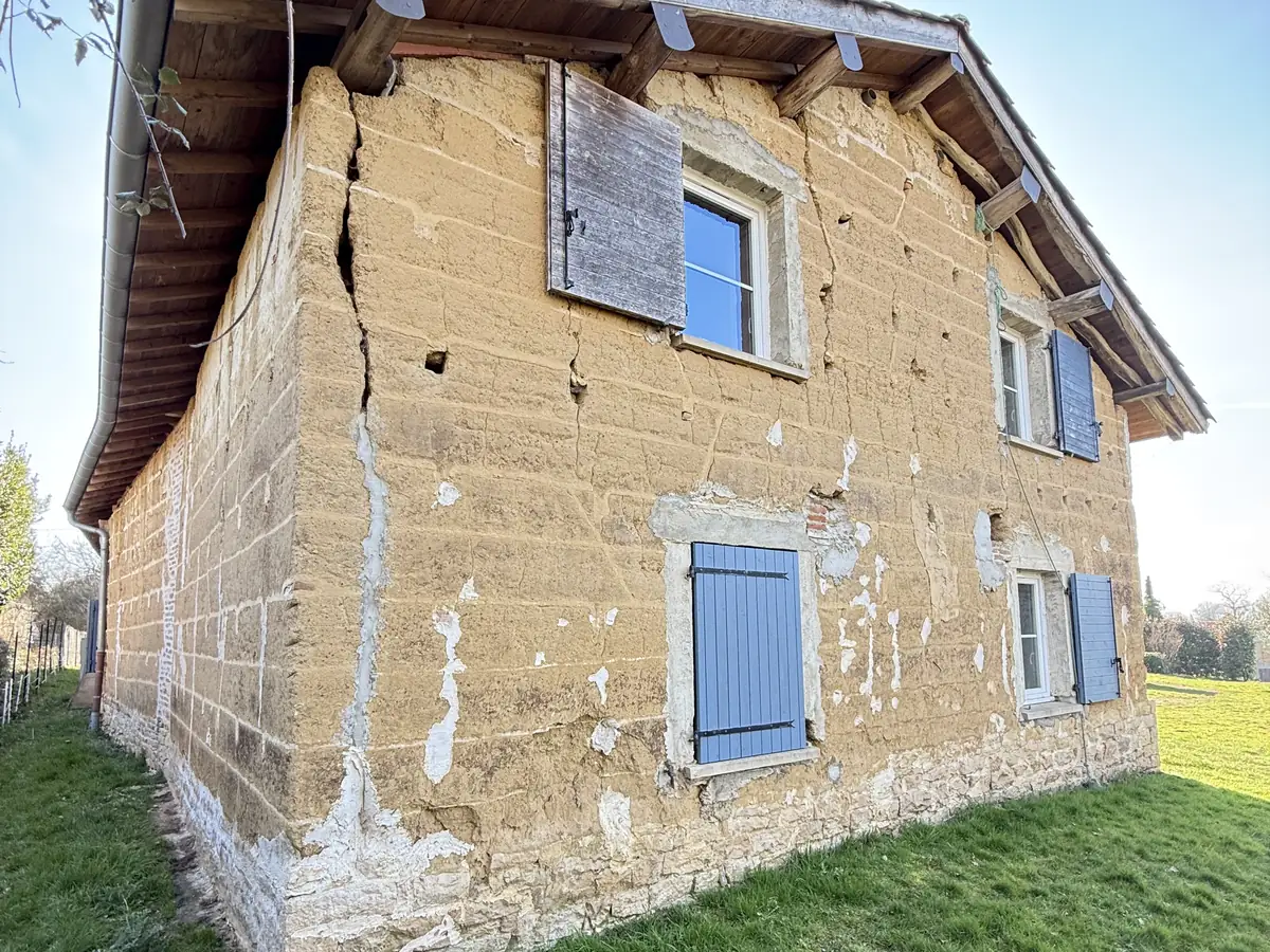 Maison en pisé à Lent, enduit tombé par plaques, fissures apparentes