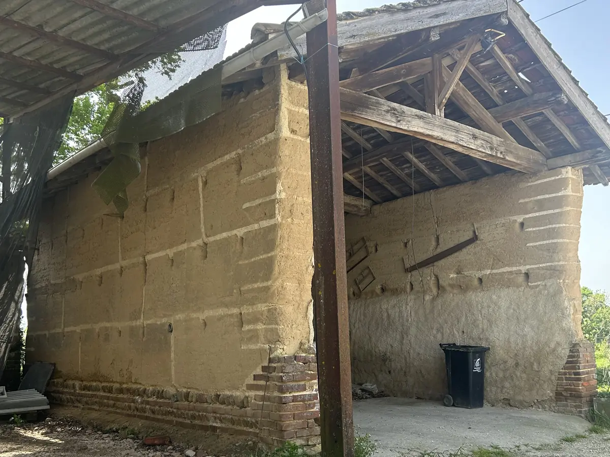 Mur en pisé à nu sous un auvent de grange, avant enduit