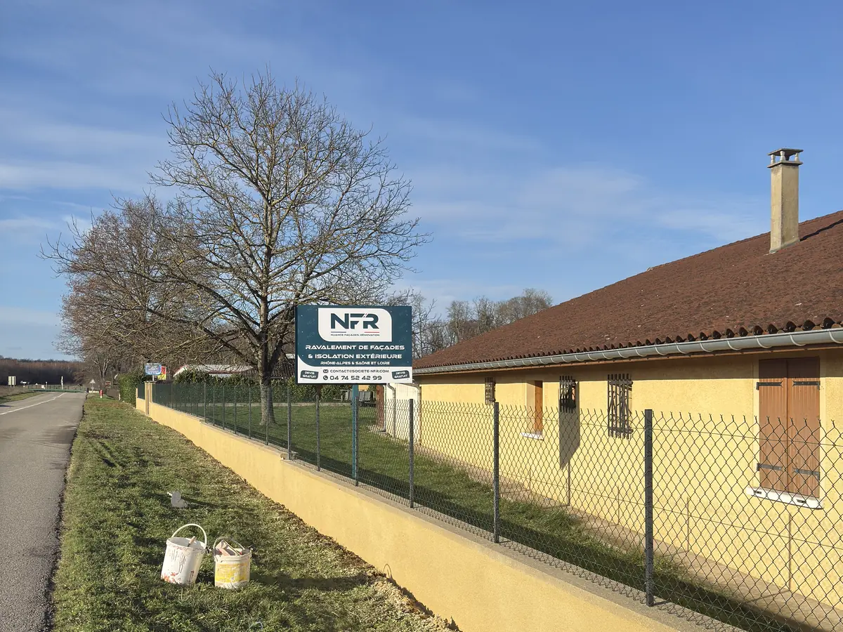 Maison et mur de clôture repeints en jaune à Montagnat, panneau Une réalisation NFR sur le grillage