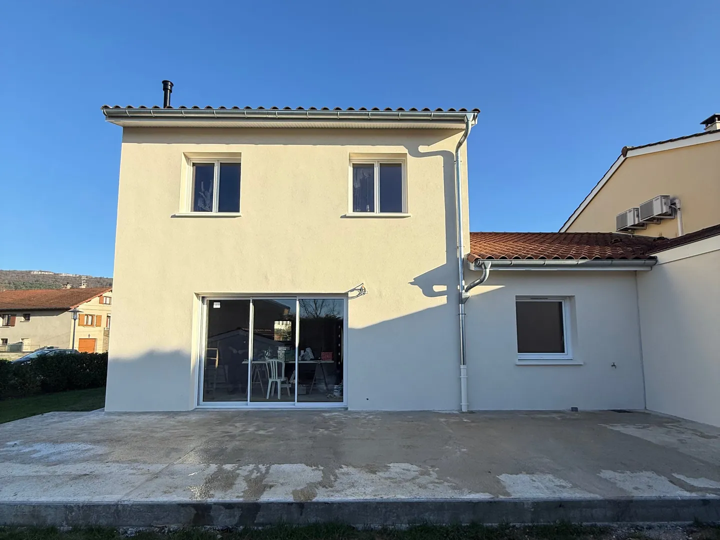 Façade arrière de la maison ravalée à Ceyzériat, enduit clair et baie vitrée sur la terrasse