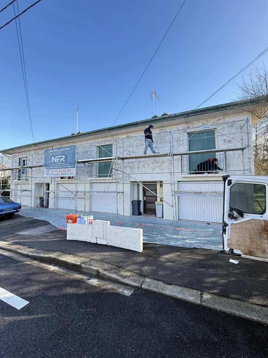 Deux artisans NFR sur échafaudage appliquent l'enduit de façade d'une maison mitoyenne, fourgon de chantier au premier plan